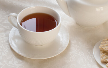 A white teapot, a cup of black tea and sweets are on the table.