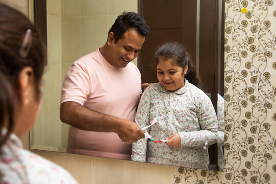 Father and daughter squeezing toothpaste on toothbrushes