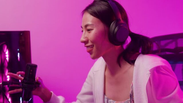 Close-up Young Asia female sit on gaming chair wear headset focus concentration pc screen competition tournament championship in game room at house. Gamer girls raise fist gloats over winning e sport.