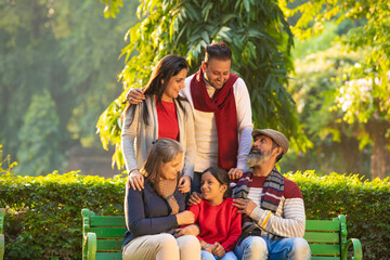 happy Indian family sitting at park in winter wear or warm clothes. - Powered by Adobe