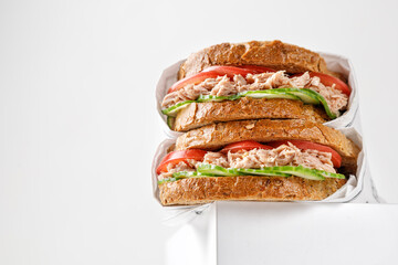 low view of two delicious tuna sandwiches with tomato and cucumber in paper on white box