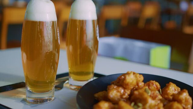 two glasses of beer lager beverage drinks sparkling with a plate of food dish ssnackin a restaurant cafe party with a waiter on background