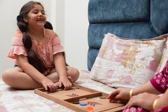 Little girl playing fast sling puck with her mother on bed
