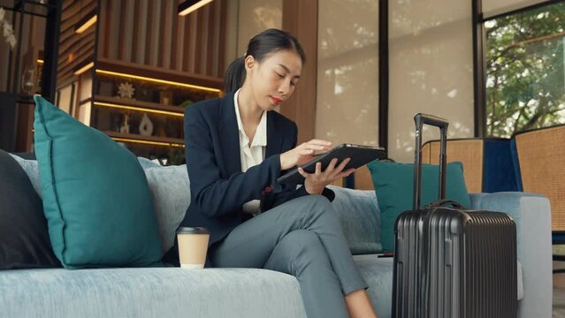 Youth Asia Female passenger formal suit sit sofa use digital tablet online booking hotel ticket for business travel trip at lounge transit international airport. Airline and Hotel facility concept.