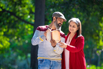 Senior Indian man and woman reading book at park.
