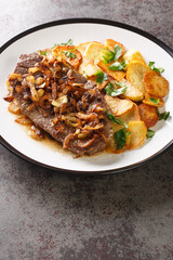 Zwiebelrostbraten a german steak with onions and fried potatoes Bratkartoffeln closeup on the plate on the table. Vertical