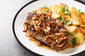 German beef steak Rostbraten with onion and fried potatoes closeup on the plate on the table. Horizontal