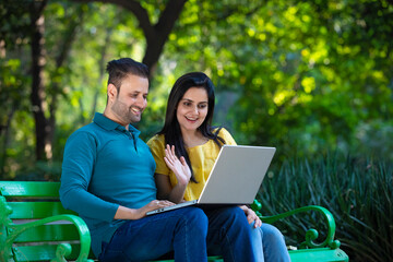 Young indian couple using laptop at park.