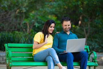 Young indian couple using laptop at park.