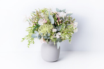 Beautiful flower arrangement of delicate pink flowers, Eucalyptus leaves, Queen Anne's Lace, and lush green foliage, in a grey vase, with a white background.