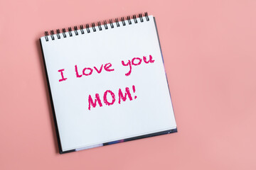 Text words I love you mom on sheet of paper. Happy mothers day concept. Pastel pink background.