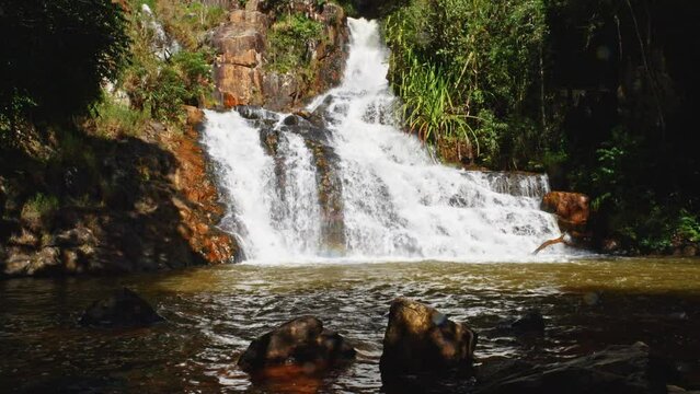 A breathtaking slow-motion shot of the Datanla Waterfall in Da Lat, Vietnam. Static shot highlights natural beauty of waterfall with rocks in the foreground. Tranquil and serene view of natural wonder