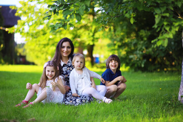 Fototapeta premium Young large family on a summer morning walk. Beautiful mother with children is playing in the park.