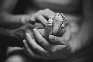 The hands of the mother and father hold the feet of their baby. 