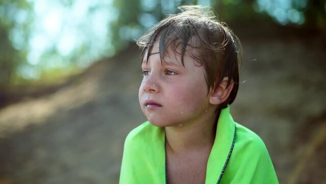 cute wet little boy wrapped with towel trembling from cold after swimming in forest lake