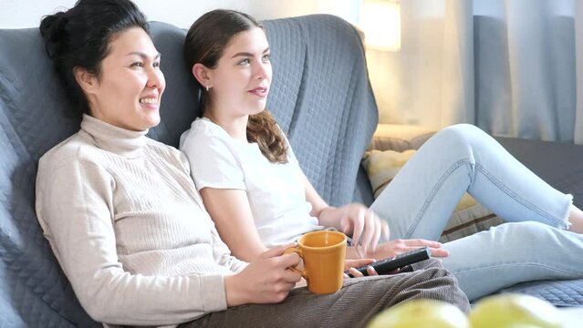 Smiling young loving couple sitting on couch at home watching funny movie together