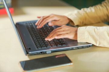 picture of an  Asian young woman's hands are typing using a laptop computer on the table