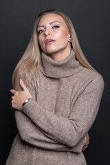 Studio portrait of beautiful brunette woman with day make-up and cozy beige sweater. Model hugging herself with hands and looking at the camera. Toned image with blue color