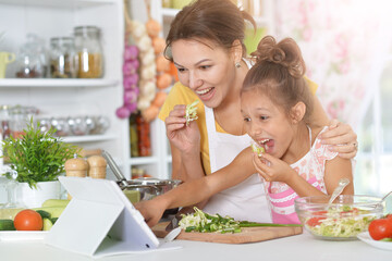 Cute little girl with mother cooking together at kitchen table