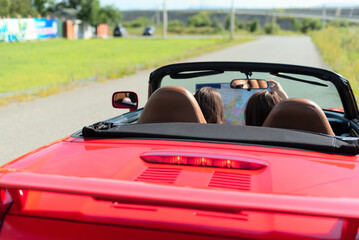 Fototapeta na wymiar Back view of happy girls driving red cabriolet car during vacation road trip having fun together discovering new places looking to the map. Road trip travel enjoying freedom concept. Selective focus