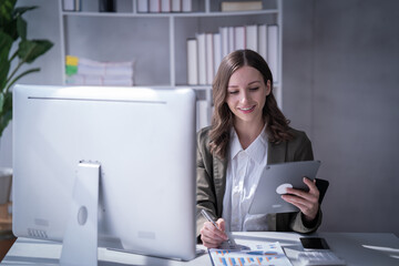 Fototapeta premium Sharing good business news. Attractive young businesswoman talking on the mobile phone and smiling while sitting at her working place in office and looking at laptop PC.