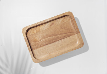 Wooden plate with palm leaf shadow on white background.