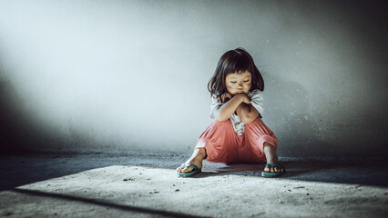 Homeless sad little child girl sitting alone on floor concrete wall background