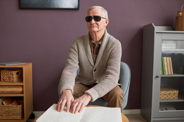 Senior blind man in eyeglasses reading a book