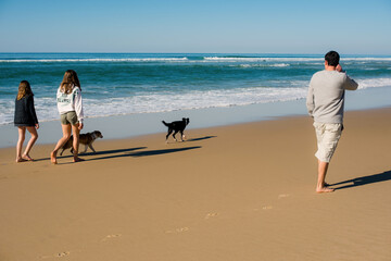 Young woman and a young girl walking and running barefoot along the edge of the beach with their puppies © Image'in