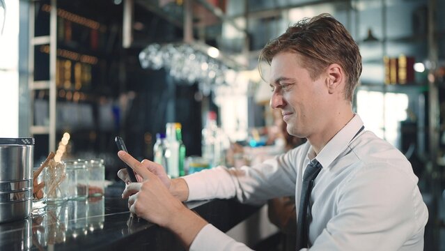 A young businessman sitting and using smartphone for chatting at the bar in the restaurant - Powered by Adobe
