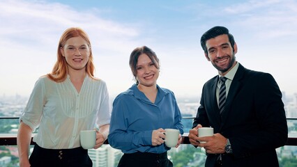 Team of young businesspeople standing and holding a cup of coffee smiling and looking at camera in the office building