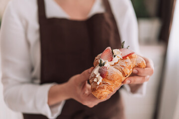 Obraz na płótnie Canvas Confectioner in brown apron holding a croissant with strawberries.