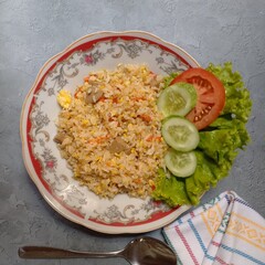 Top view of fried rice “nasi goreng” with slice of cucumber, tomatoe and lettuce at the plate of red flower motive in the kitchen