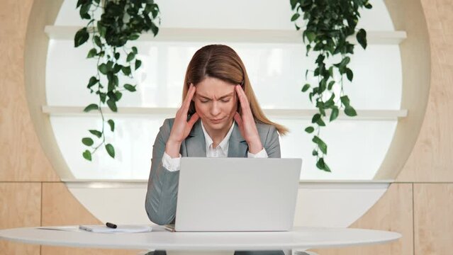Stressed adut business woman with nice appearance suffering from muscles tension, having painful head feelings due to computer overwork. Face of tired employee overwhelmed with tasks in eco office. 