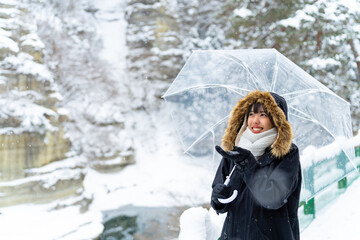  Asian woman in winter coat holding umbrella walking down footpath on forest mountain near small town in snow day. Attractive girl tourist solo travel local village in Japan on winter holiday vacation