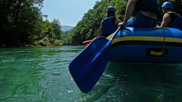 Group of tourists wearing helmets and life jackets sit on inflatable rubber boat and hold oars in their hands. Rafting on quiet section of wild mountain river Tara. Excursions in Montenegro