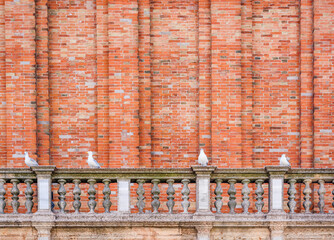 Seagulls sitting on the balcony of St. Mark's Bell Tower against a red brick wall