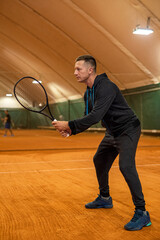 Full length portrait of agile male athlete playing tennis on indoor court.