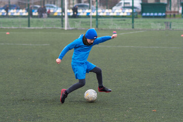 children's football, a boy of European race is studying on a green field with a ball in a blue uniform