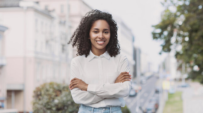 Young businesswoman in a city looking at camera, African-american student girl portrait, Young woman with crossed arms smiling, People, enjoy life, student lifestyle, city life, business concept
