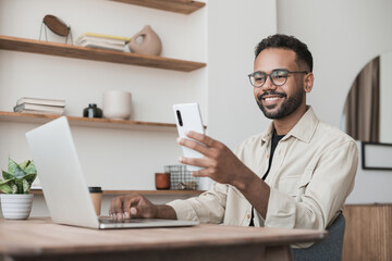 Young handsome man using smart phone and laptop at home. Businessman or student working on computer and texting smartphone. Freelance, education and technology concept