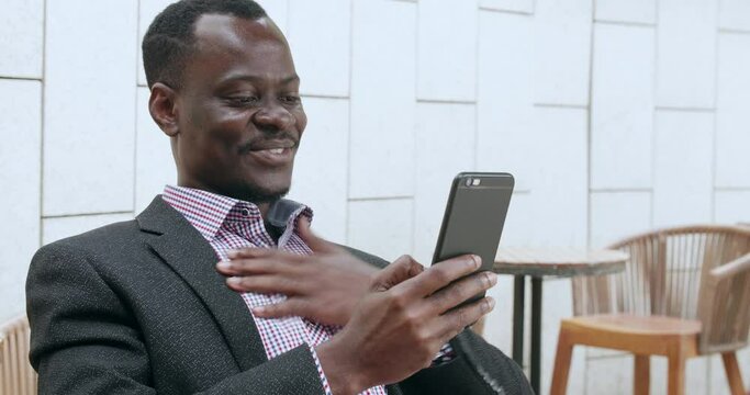 One young Happy African businessman holding mobile phone video chatting with friend in the urban cafe
