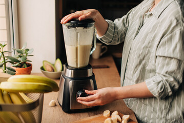 Woman blending spinach, berries, bananas and almond milk to make a healthy green smoothie