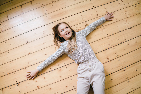 Thoughtful girl with arms outstretched lying on floor at home