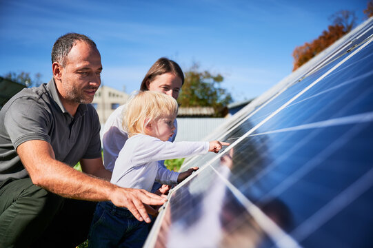 Enthusiastic father showing potential of alternative energy. Contemporary family looking at new solar station they bought. Side view of happy parents and interested child next to solar panels.