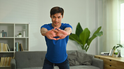 Fototapeta na wymiar Handsome sporty man exercising and doing squats in living room. Sport and healthy lifestyle concept