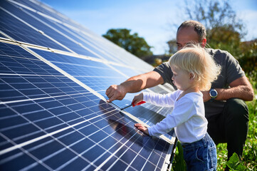 Man showing his small child the solar panels during sunny day. Father presenting to son modern...