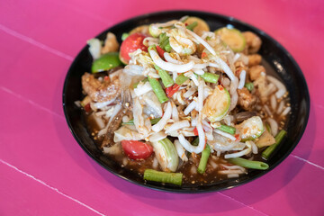 Spicy salad that is colorful and tasty, with pickled fish, long beans, bean sprouts, pork caps, crispy fish, tomatoes, and pepper. Ready to eat on wood pink table.