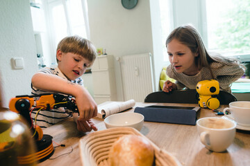 Girl looking at brother playing with robotic model at home