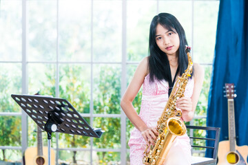 Young woman saxophonist with an instrument stands by the window. Cozy home interior. Concept of...
